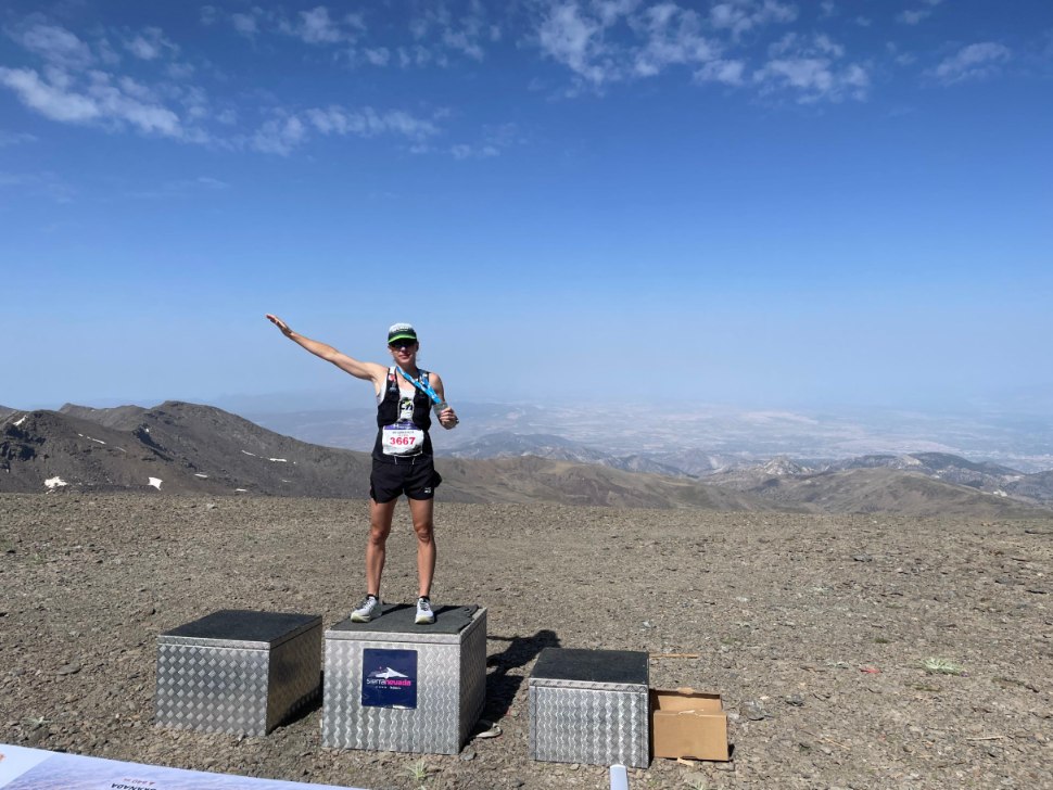Ana Gay standing on a podium box on a bare mountain top, pointing at the horizon